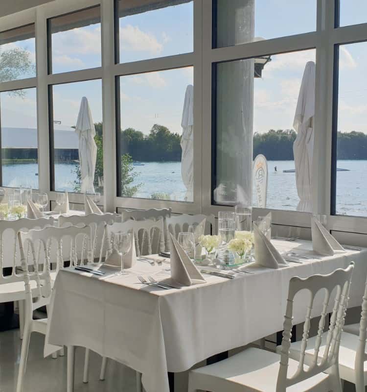 Ein Restaurant mit weißen Tischen und Stühlen mit Blick auf einen See.