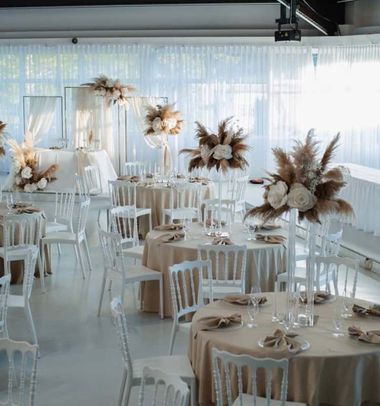 Ein Hochzeitsempfang in Weiß und Beige mit weißen Tischen und Stühlen.