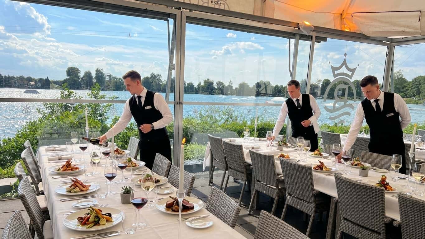 Professioneller Service eines Gourmet-Gerichts an einem elegant gedeckten Tisch mit Seeblick