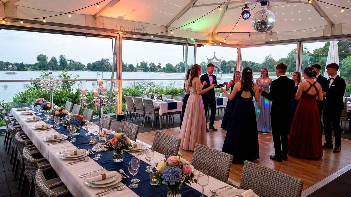 Junge Menschen in festlicher Kleidung tanzen auf der Seeterrasse unter Lichterketten